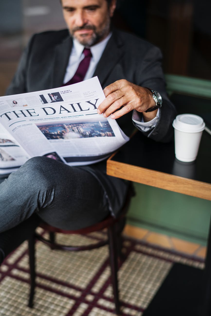 man sitting on red wooden chair while reading newspaper